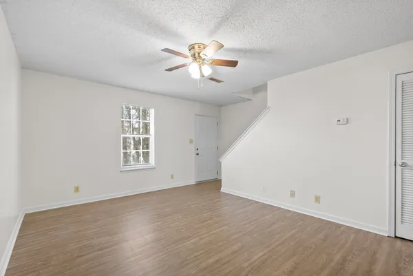 an empty room with wooden floor chandelier fan and windows