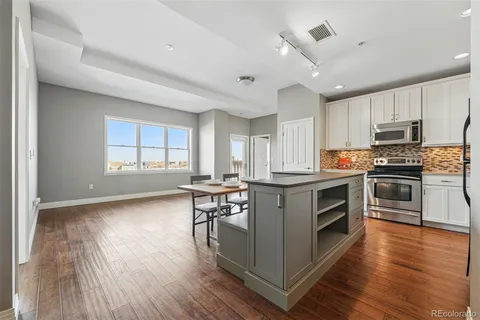 a kitchen with granite countertop a stove a sink dishwasher a refrigerator and a dining table with wooden floor