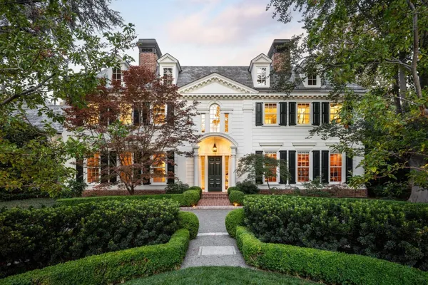 a front view of a brick house with a yard and large trees