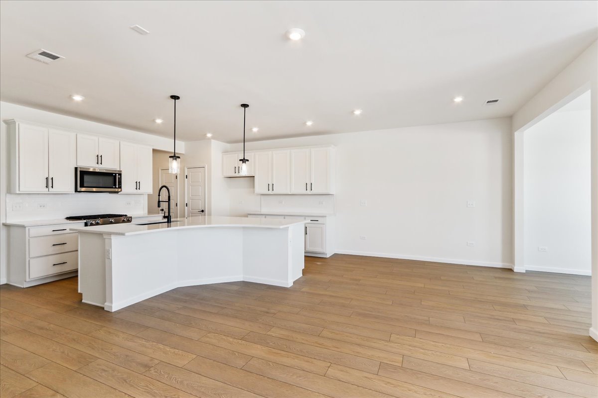 667 Switchgrass Way, Unit 62003 Bolingbrook, IL 60490 - Photo 11 of 33 a large white kitchen with kitchen island a sink a center island stainless steel appliances and a cabinets