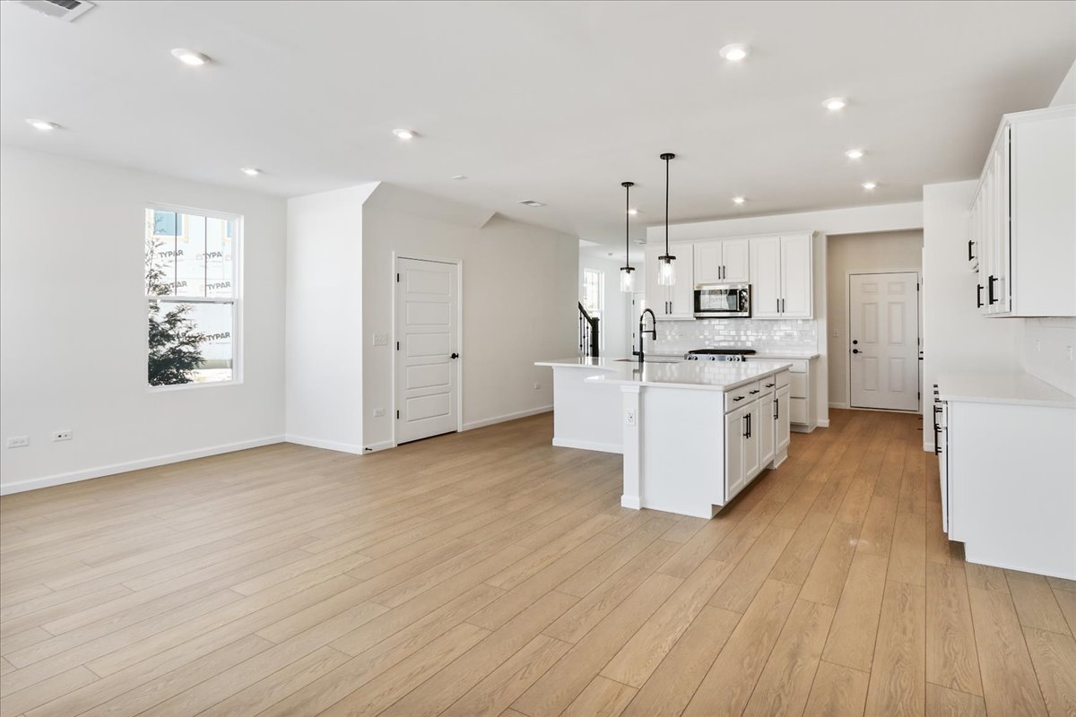 667 Switchgrass Way, Unit 62003 Bolingbrook, IL 60490 - Photo 9 of 33 a large kitchen with stainless steel appliances granite countertop a large center island a stove a refrigerator cabinets and a wooden floor