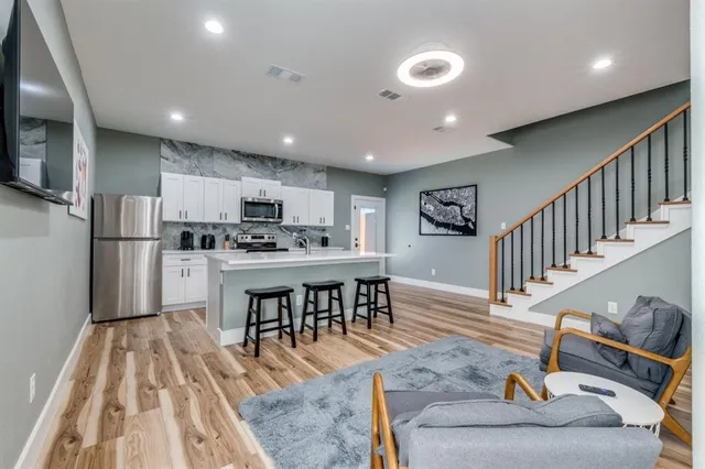 a kitchen with stainless steel appliances kitchen island granite countertop a refrigerator a stove a sink a dining table and chairs with wooden floor