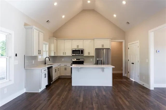 a kitchen with stainless steel appliances a sink a stove a refrigerator cabinets and a wooden floor