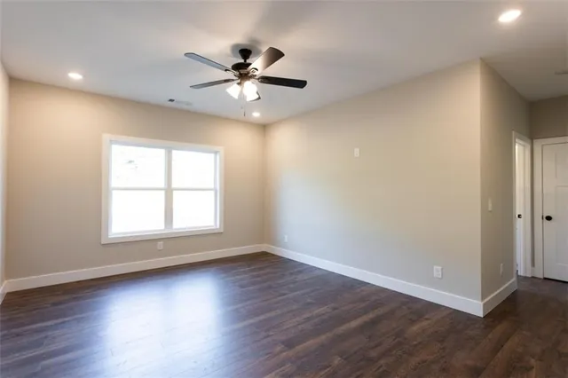 an empty room with wooden floor fan and windows
