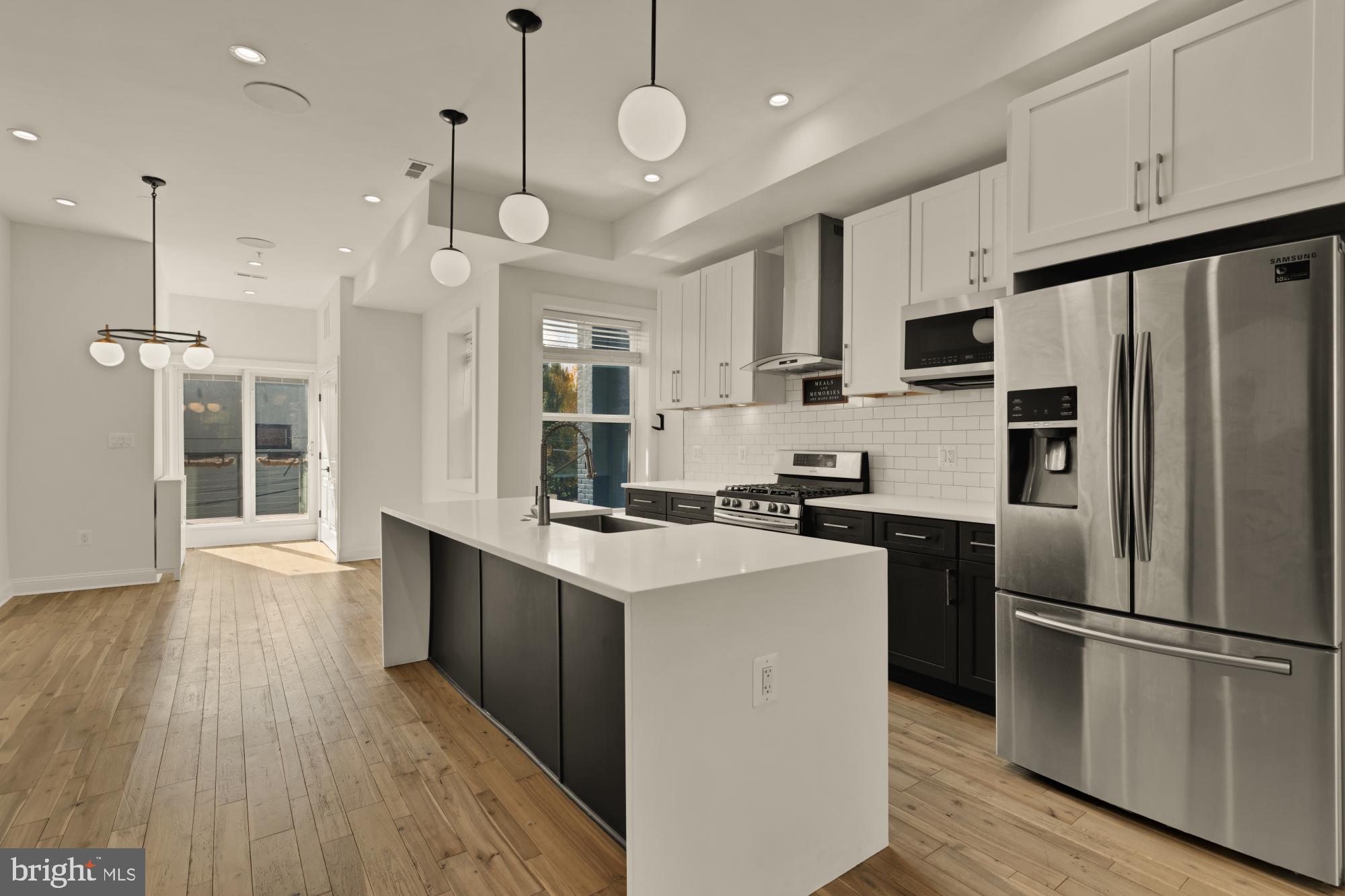 a kitchen with stainless steel appliances a stove a refrigerator a sink and white cabinets with wooden floor