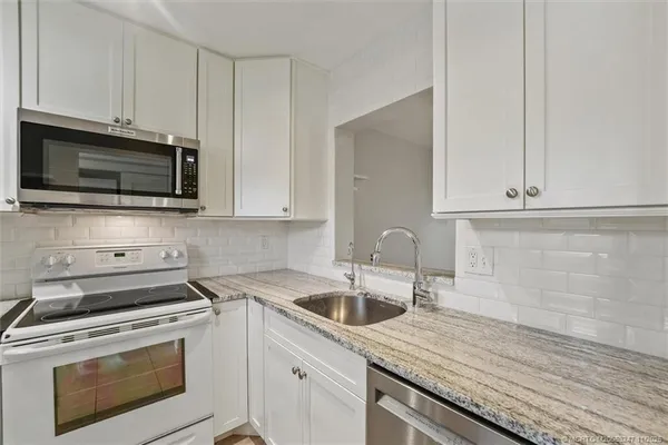 a kitchen with granite countertop white cabinets sink and stainless steel appliances
