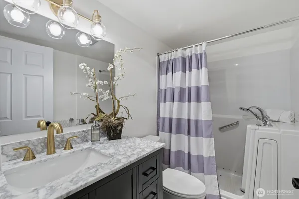 a bathroom with a granite countertop sink a toilet a mirror and shower curtain