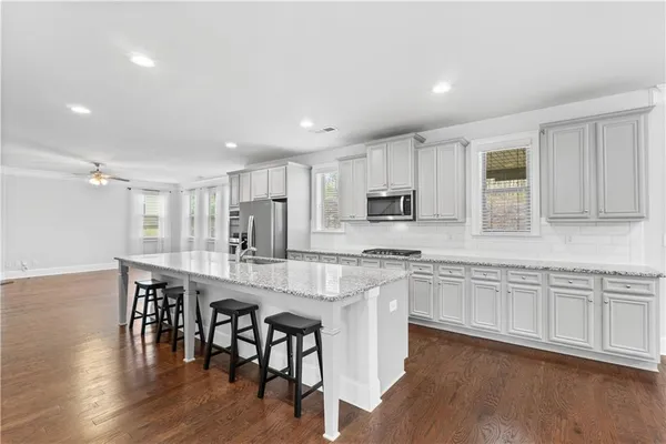 a large white kitchen with stainless steel appliances granite countertop a stove a sink a dining table and chairs
