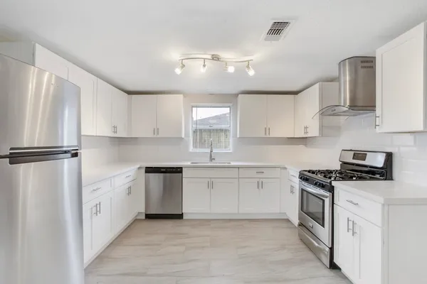 a kitchen with stainless steel appliances granite countertop a sink a stove a refrigerator and white cabinets