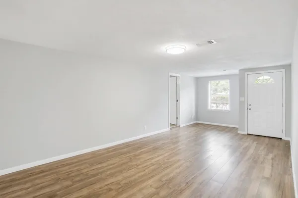 a view of an empty room with wooden floor and window