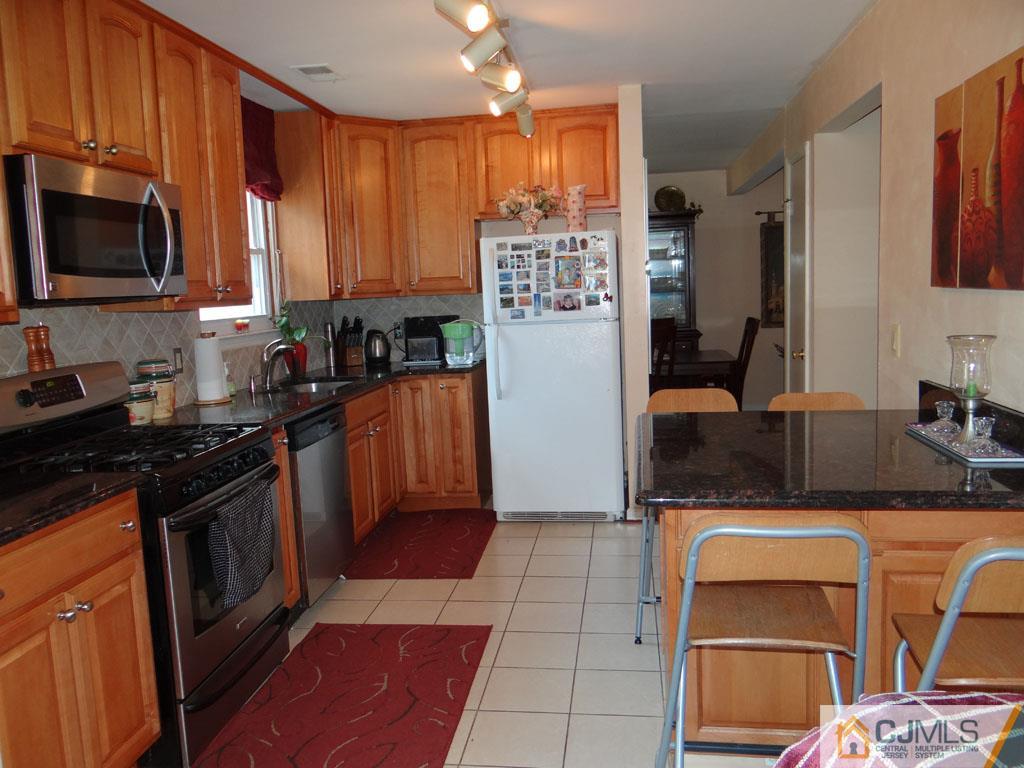 92 Woodbury Road Edison, NJ 08820 - Photo 3 of 16 a kitchen with stainless steel appliances granite countertop a stove top oven a sink dishwasher and wooden cabinets