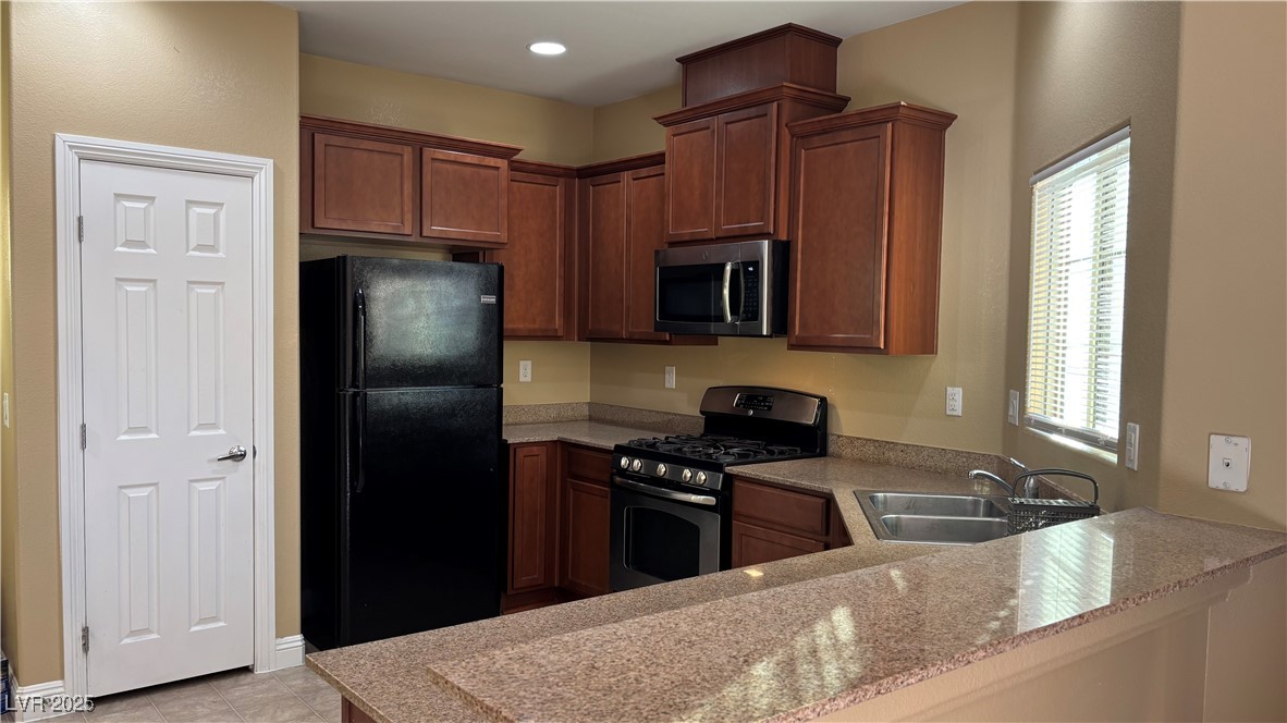 9473 Alma Ridge Avenue Las Vegas, NV 89178 - Photo 6 of 35 Kitchen featuring stainless steel appliances, light stone countertops, light tile patterned floors, and brown cabinets
