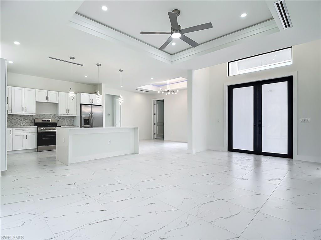 2707 36th Avenue Southeast Naples, FL 34117 - Photo 12 of 50 Unfurnished living room with light marble finish flooring, a tray ceiling, a chandelier, recessed lighting, and ceiling fan
