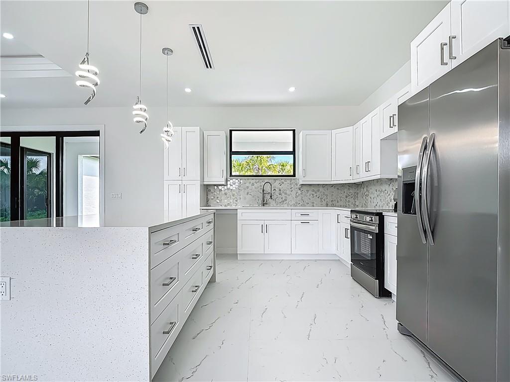 2707 36th Avenue Southeast Naples, FL 34117 - Photo 16 of 50 Kitchen with appliances with stainless steel finishes, backsplash, light marble finish floors, recessed lighting, and hanging light fixtures