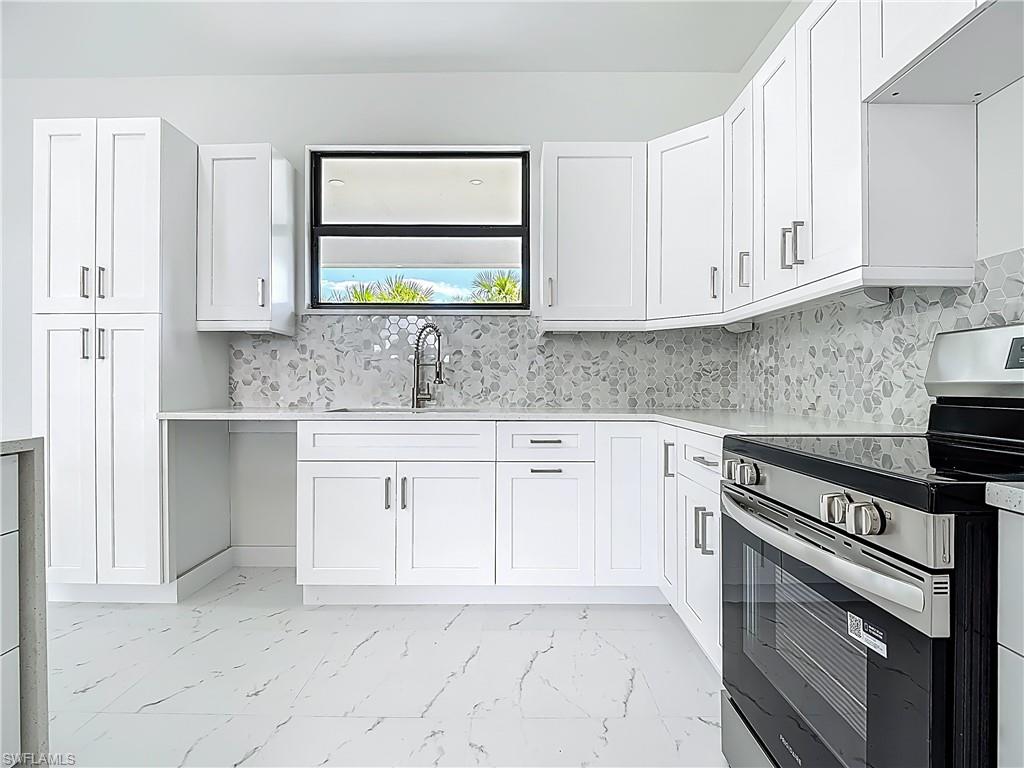 2707 36th Avenue Southeast Naples, FL 34117 - Photo 18 of 50 Kitchen with stainless steel range with electric cooktop, light marble finish floors, white cabinetry, and light countertops