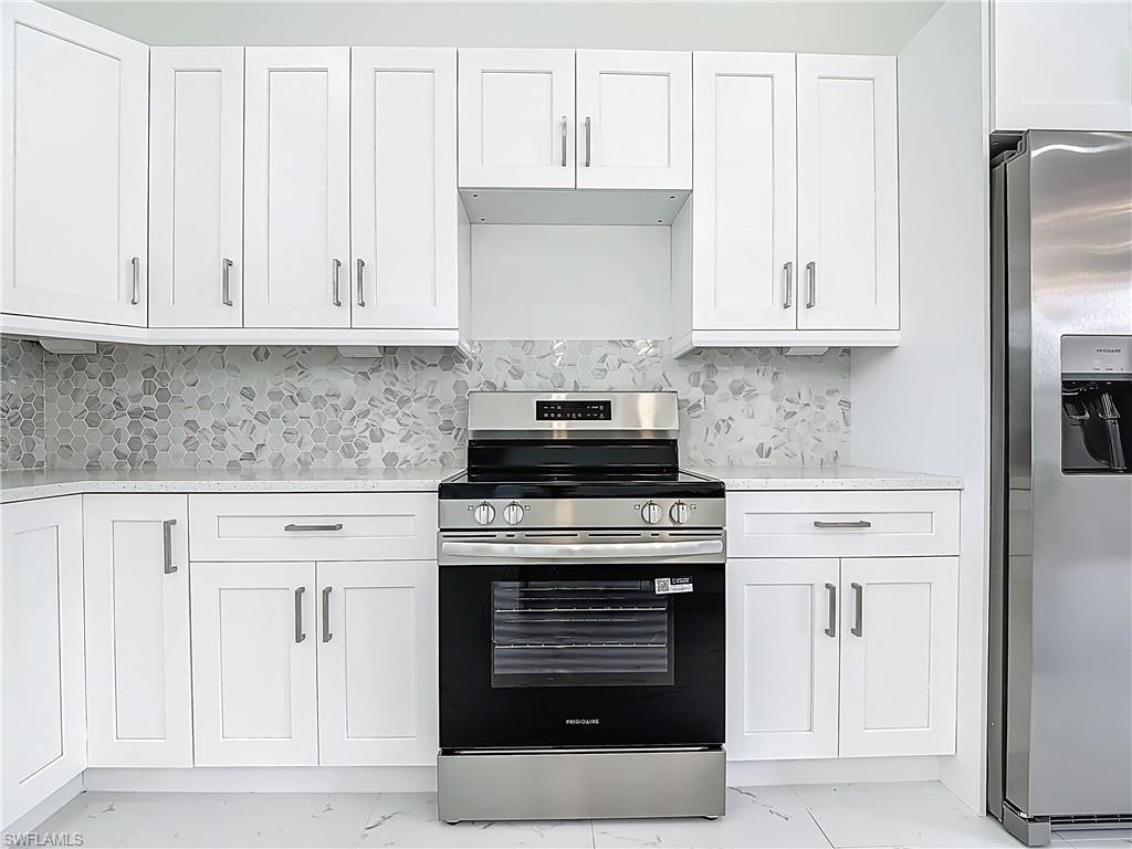 2707 36th Avenue Southeast Naples, FL 34117 - Photo 19 of 50 Kitchen with light marble finish flooring, appliances with stainless steel finishes, white cabinets, and decorative backsplash