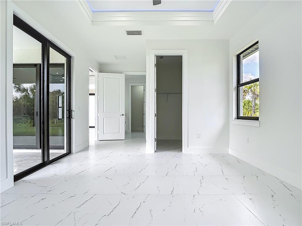 2707 36th Avenue Southeast Naples, FL 34117 - Photo 29 of 50 Unfurnished bedroom with light marble finish floors, access to outside, a tray ceiling, crown molding, and a closet