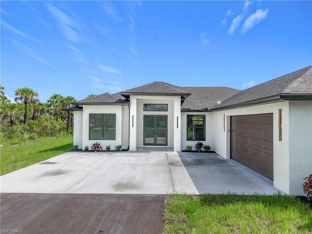 2707 36th Avenue Southeast Naples, FL 34117 - Photo 4 of 50 Prairie-style house featuring stucco siding, an attached garage, roof with shingles, french doors, and concrete driveway