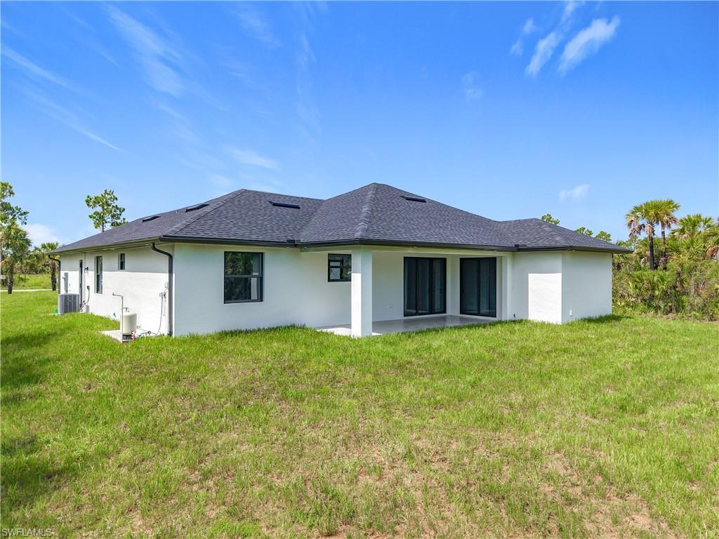 2707 36th Avenue Southeast Naples, FL 34117 - Photo 47 of 50 Rear view of property featuring stucco siding, a lawn, and roof with shingles