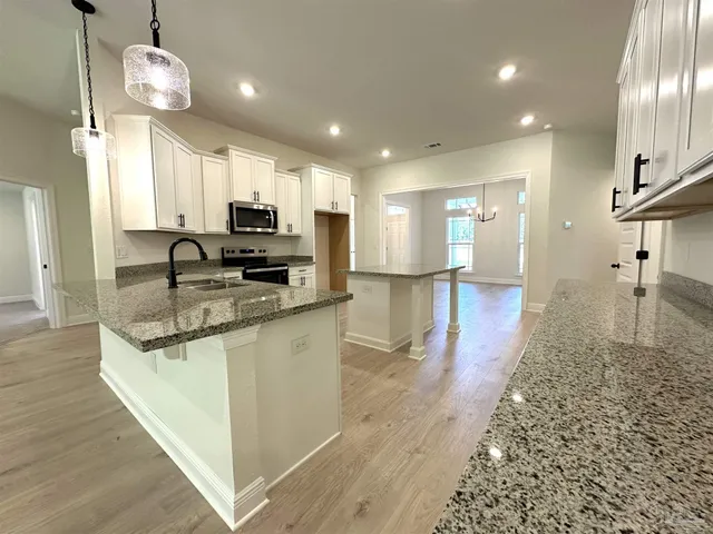 a view of a kitchen with kitchen island granite countertop wooden floor stainless steel appliances and cabinets