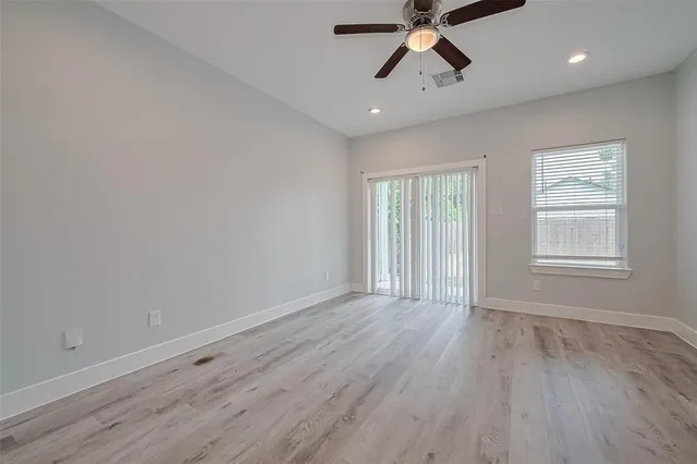 an empty room with wooden floor ceiling fan and windows