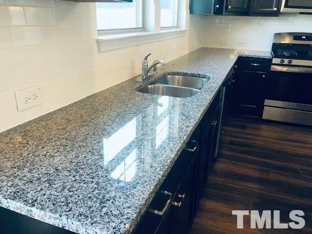 a kitchen with granite countertop a sink a stove and a wooden cabinets