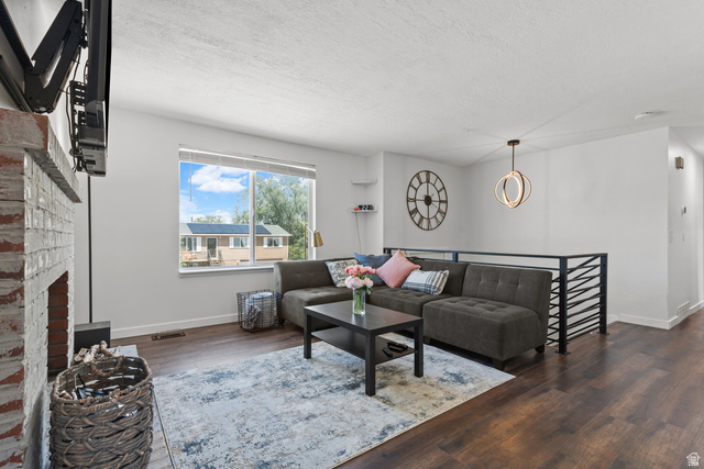 3951 Brixton Road Salt Lake City, UT 84129 - Photo 8 of 22 Spacious living area featuring rich wood-finish flooring, a white-painted brick fireplace, a large picture window, a modern pendant light fixture, and a contemporary metal railing