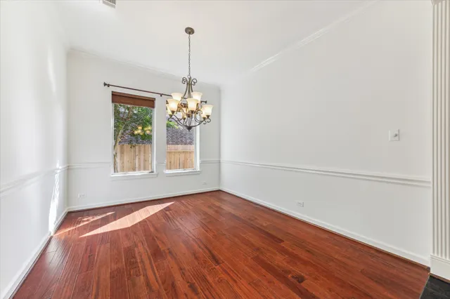 a view of an empty room with chandelier and wooden floor
