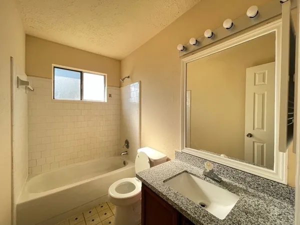 a bathroom with a granite countertop sink mirror vanity bathtub and toilet