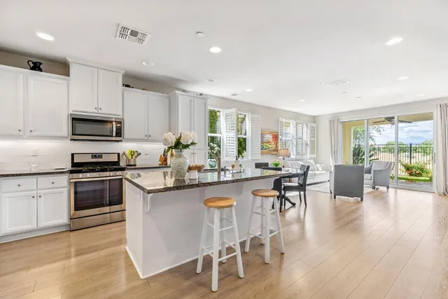 a kitchen with stainless steel appliances granite countertop a stove top oven a sink dishwasher a dining table and chairs with wooden floor