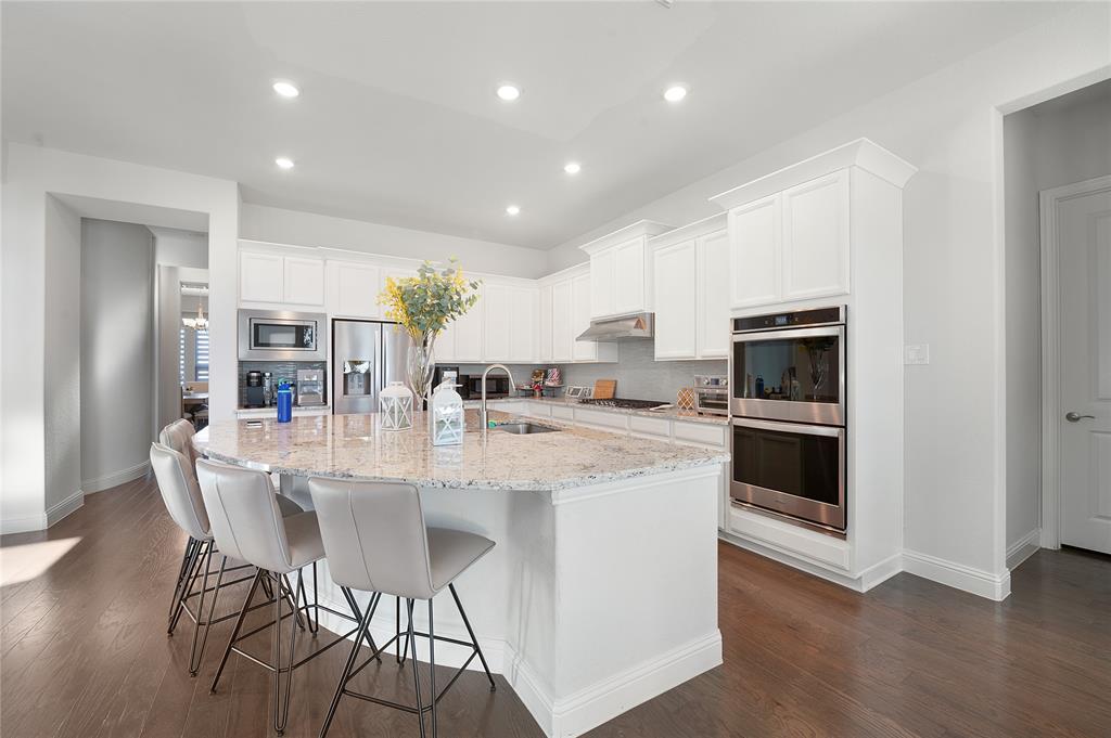 1510 Chisholm Trail Prosper, TX 75078 - Photo 11 of 32 a kitchen with stainless steel appliances kitchen island granite countertop a stove a microwave a sink a refrigerator and white cabinets with wooden floor