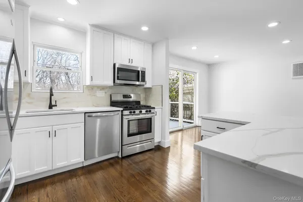 a kitchen with stainless steel appliances white cabinets a sink a stove a microwave a center island and a window