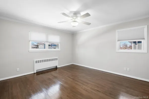 a view of an empty room with wooden floor and a ceiling fan