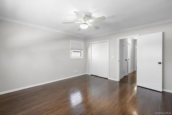 a view of an empty room with wooden floor and a ceiling fan
