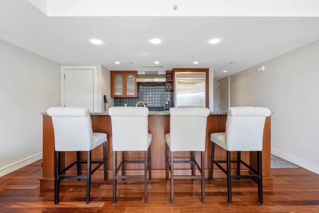 2 Battery Wharf, Unit 2503 Boston, MA 02109 - Photo 9 of 23 a kitchen with stainless steel appliances kitchen island granite countertop a dining table chairs and a refrigerator