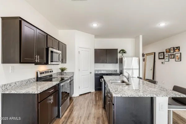 a kitchen with stainless steel appliances kitchen island granite countertop a refrigerator a stove top oven a sink dishwasher and wooden floor
