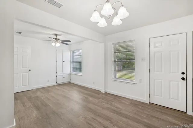 an empty room with wooden floor chandelier fan and windows