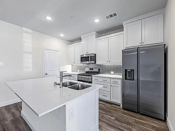 a kitchen that has a refrigerator a stove and white cabinets with wooden floor