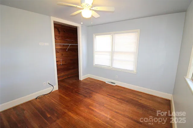 an empty room with wooden floor fan and windows