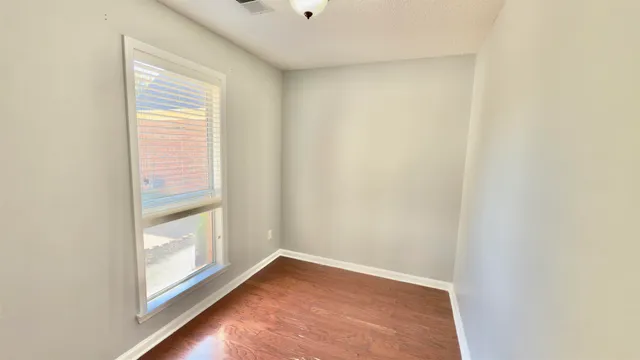 an empty room with wooden floor chandelier fan and windows