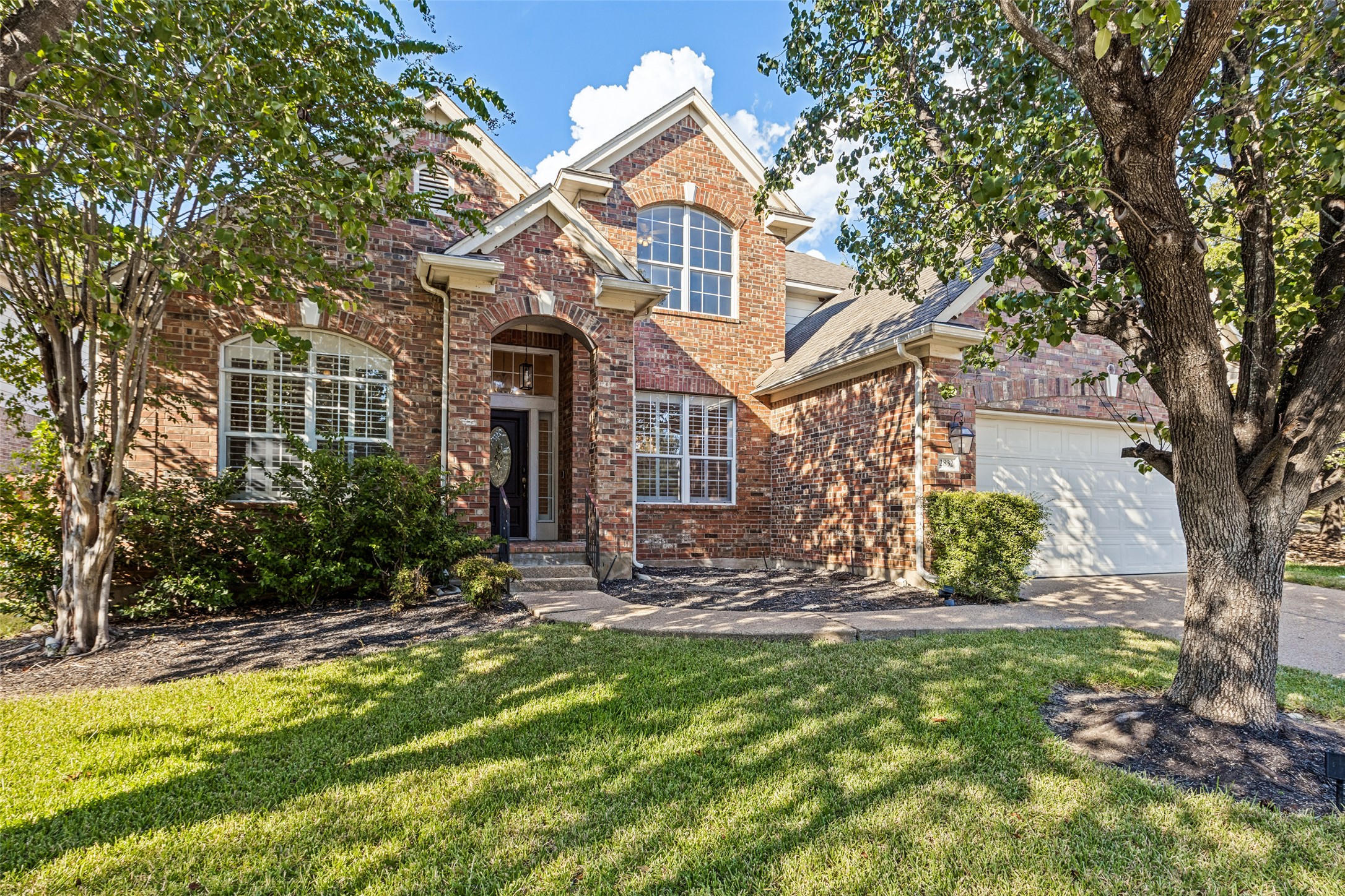 2832 Grimes Ranch Road Austin, TX 78732 - Photo 1 of 23 Mature trees frame a classic brick exterior with multi-paned windows and a two-car garage.