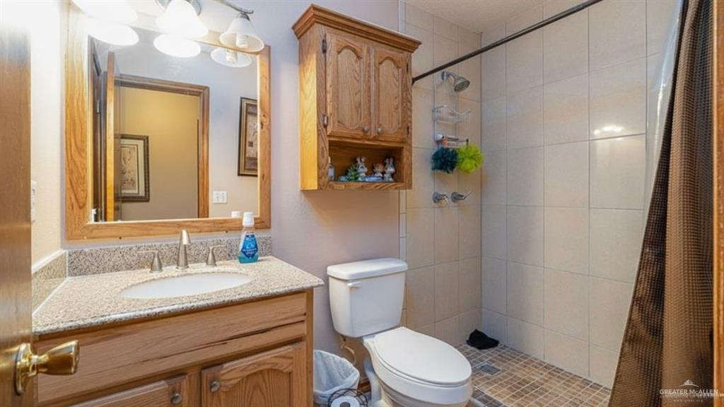 1409 Valencia Avenue Pharr, TX 78577 - Photo 10 of 11 a bathroom with a granite countertop sink toilet a mirror a vanity and shower