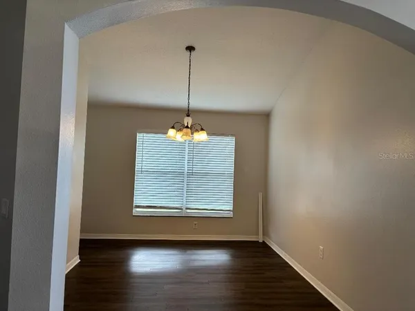 an empty room with wooden floor chandelier fan and windows