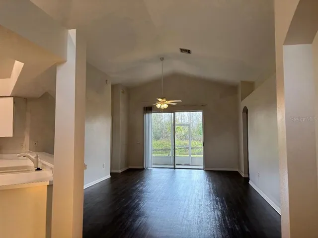 an empty room with wooden floor chandelier fan and windows
