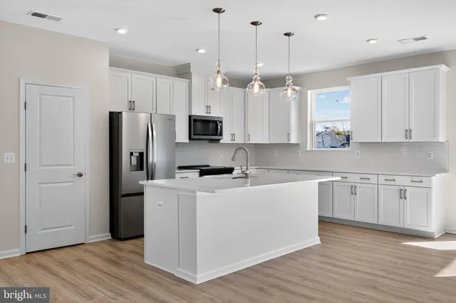 a kitchen with stainless steel appliances granite countertop a refrigerator a sink dishwasher a stove and white cabinets with wooden floor