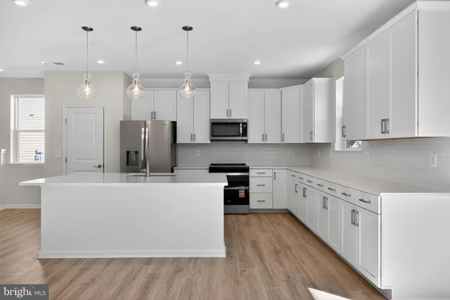 a large kitchen with stainless steel appliances granite countertop a refrigerator a stove a sink and white cabinets with wooden floor