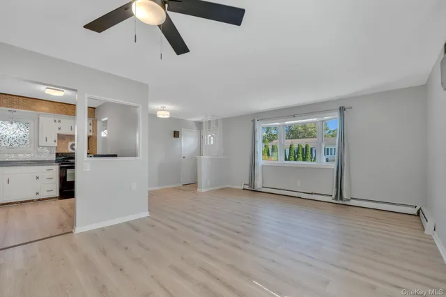 a view of an empty room with wooden floor and a kitchen