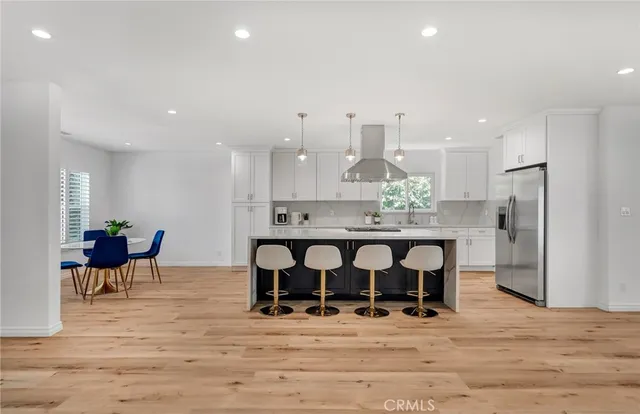 a kitchen with stainless steel appliances kitchen island granite countertop a stove a refrigerator and a dining table with wooden floor