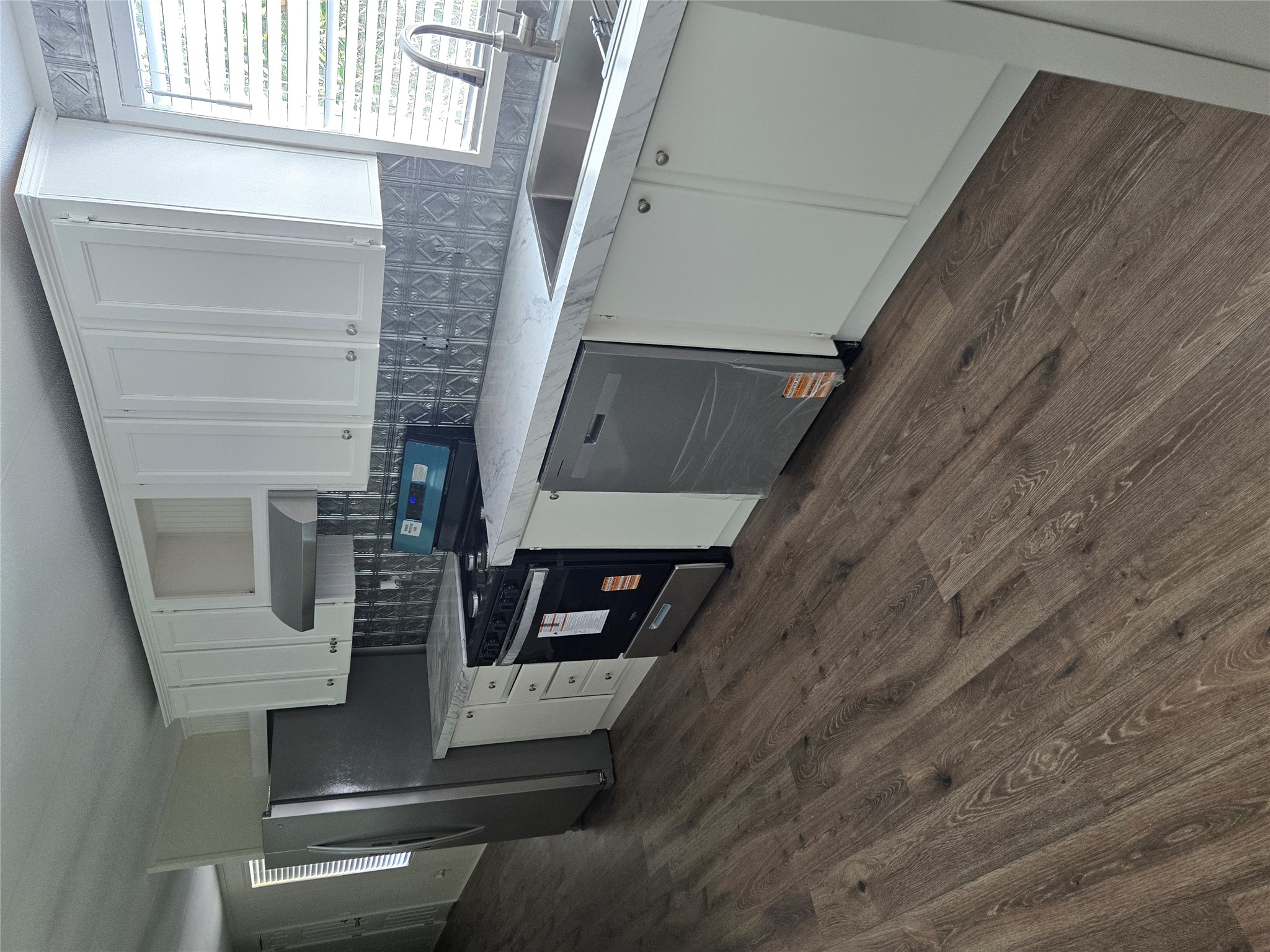 2807 Lone Tree Road Victoria, TX 77901 - Photo 2 of 12 Kitchen featuring wood-finish flooring, white cabinetry, stainless steel appliances, textured backsplash, and stone-look countertops