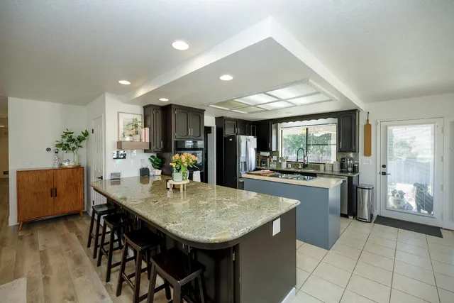 a kitchen with stainless steel appliances granite countertop a refrigerator a sink dishwasher and a dining table with wooden floor